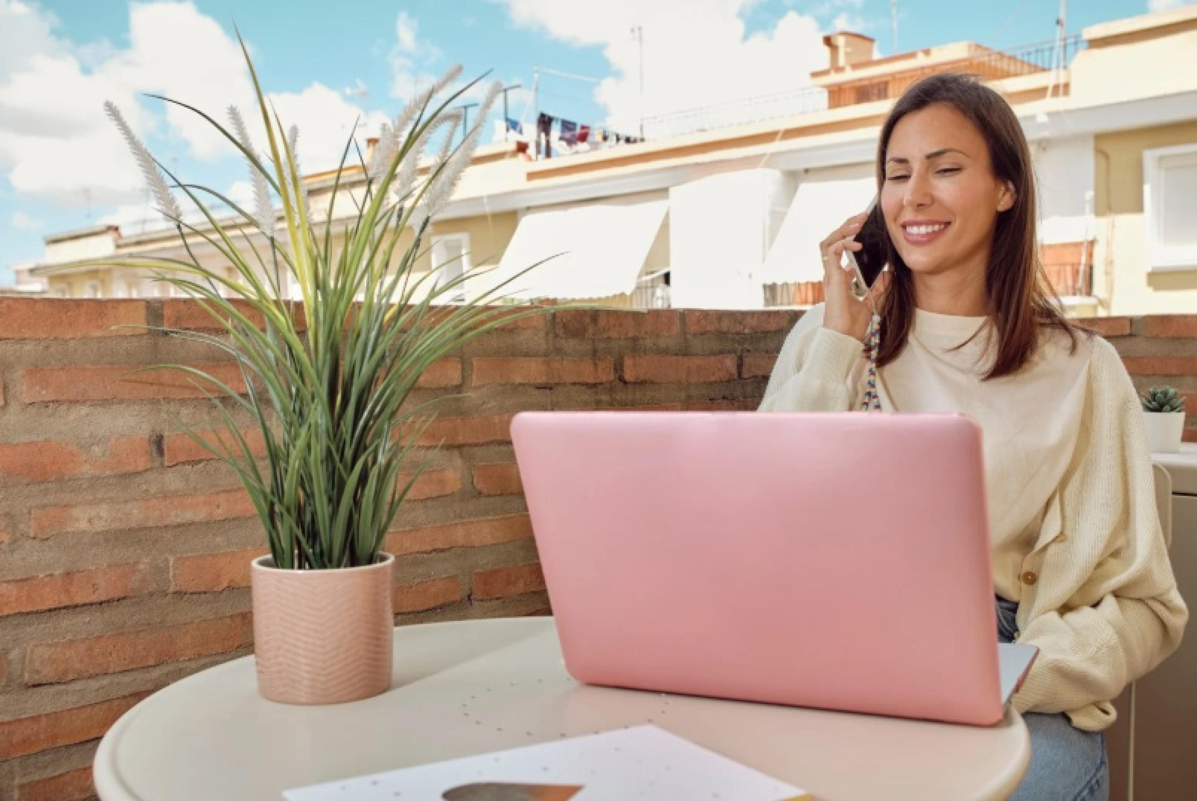 Femme qui téléphone devant son ordinateur sur son balcon